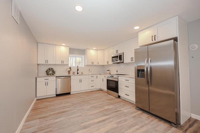 kitchen with appliances with stainless steel finishes, white cabinets, and light wood-type flooring