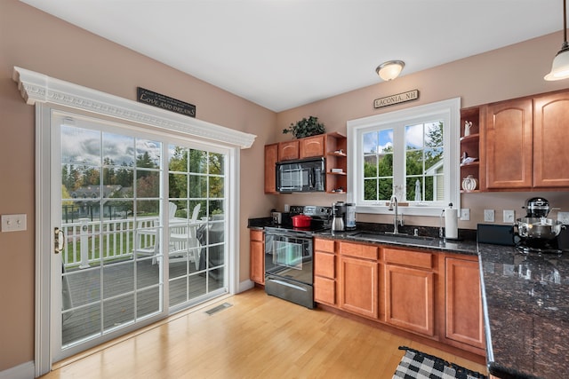 kitchen with light hardwood / wood-style flooring, dark stone countertops, sink, black appliances, and pendant lighting