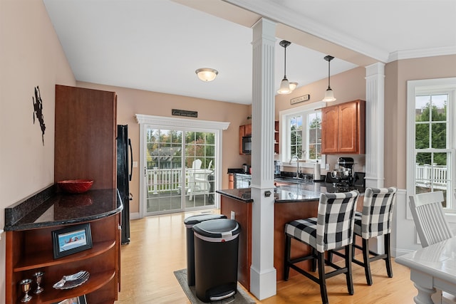 kitchen with ornate columns, kitchen peninsula, decorative light fixtures, and light wood-type flooring