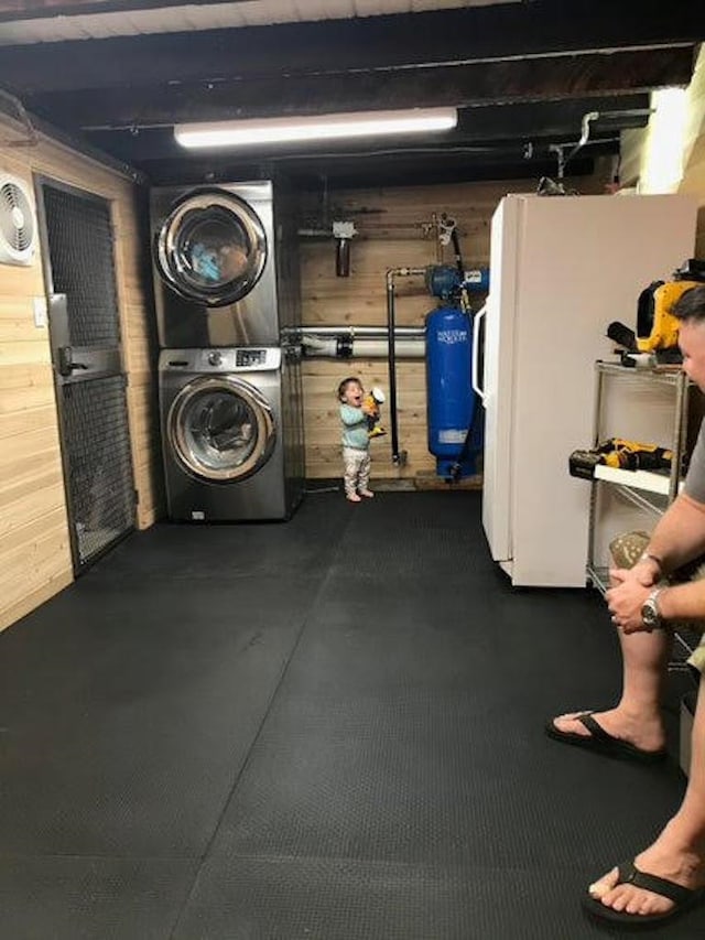 basement featuring wooden walls, white refrigerator, and stacked washing maching and dryer