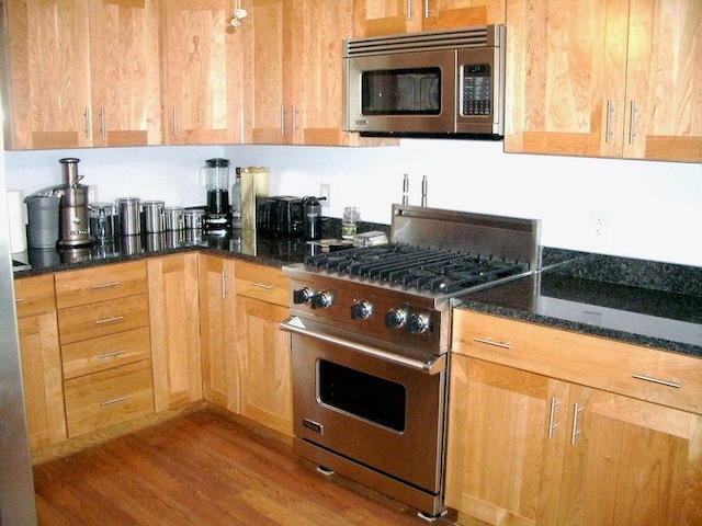 kitchen featuring stainless steel appliances, light hardwood / wood-style floors, and dark stone countertops