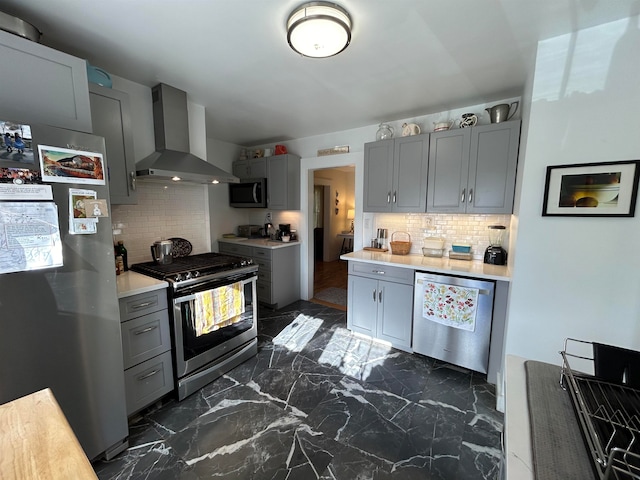 kitchen with gray cabinetry, backsplash, wall chimney exhaust hood, and appliances with stainless steel finishes