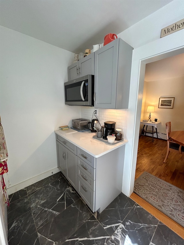 kitchen featuring dark hardwood / wood-style flooring, a baseboard radiator, gray cabinetry, and tasteful backsplash