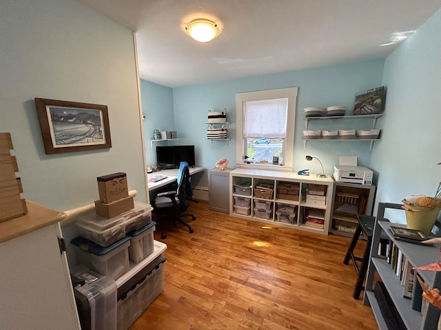 home office with light hardwood / wood-style floors and a baseboard heating unit