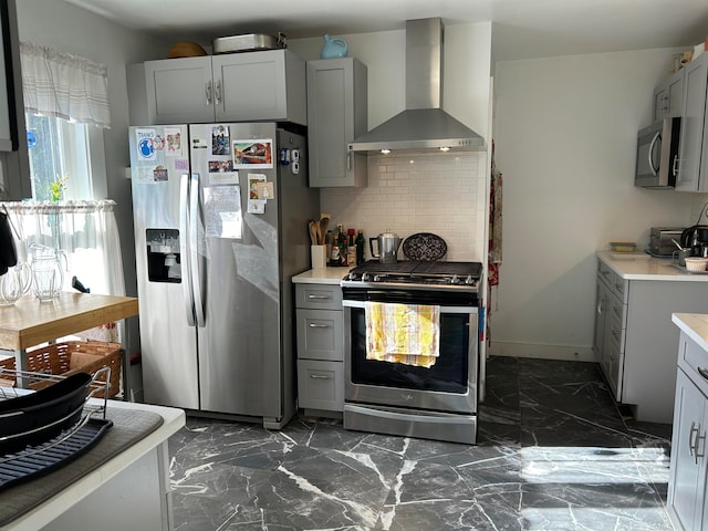 kitchen with wall chimney range hood, decorative backsplash, stainless steel appliances, and gray cabinetry