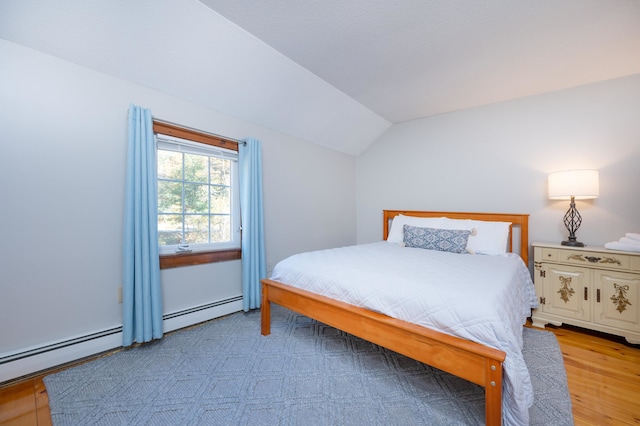 bedroom featuring vaulted ceiling, a baseboard heating unit, and light hardwood / wood-style floors