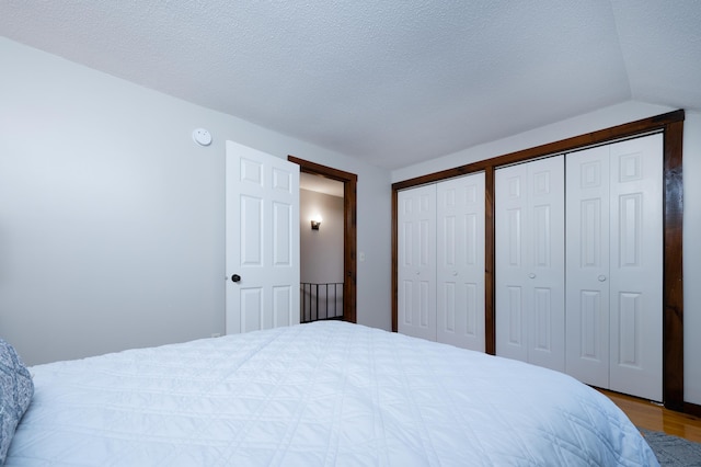 bedroom with multiple closets, a textured ceiling, hardwood / wood-style flooring, and lofted ceiling