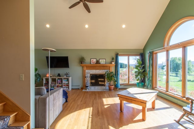 living room with a baseboard radiator, ceiling fan, a high end fireplace, high vaulted ceiling, and light wood-type flooring