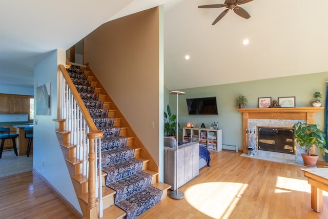 staircase featuring a tile fireplace, hardwood / wood-style floors, a baseboard radiator, high vaulted ceiling, and ceiling fan