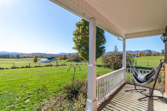 wooden deck with a mountain view, a lawn, and a rural view