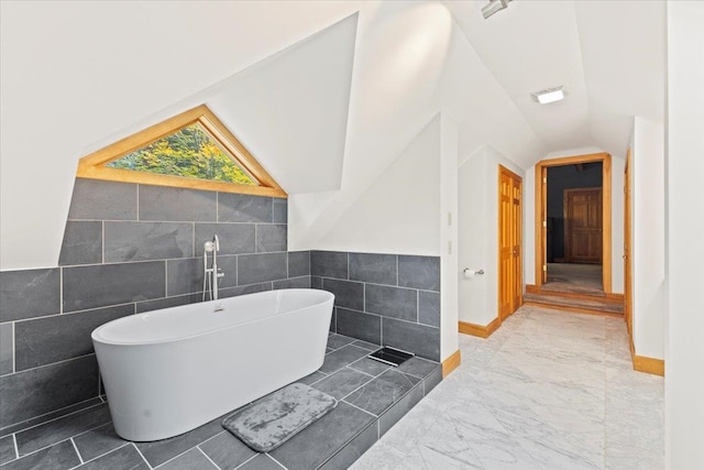 bathroom featuring lofted ceiling, a tub, and tile walls