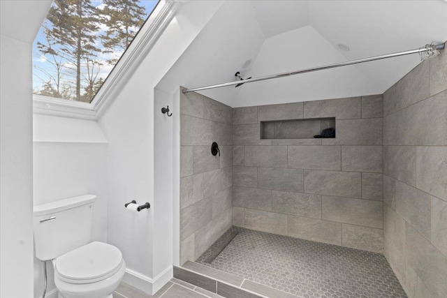 bathroom with toilet, vaulted ceiling with skylight, and a tile shower