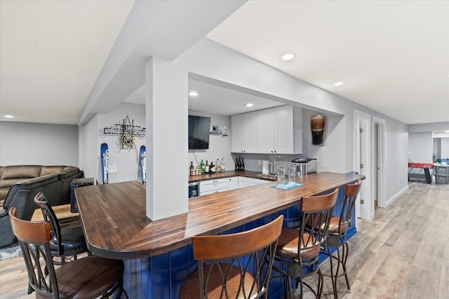 bar featuring light hardwood / wood-style flooring, white cabinetry, sink, and butcher block countertops