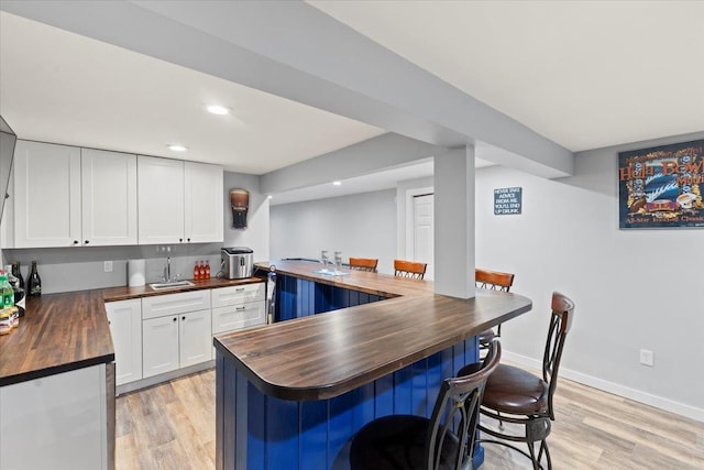 kitchen featuring wooden counters, kitchen peninsula, a kitchen bar, white cabinetry, and light hardwood / wood-style floors