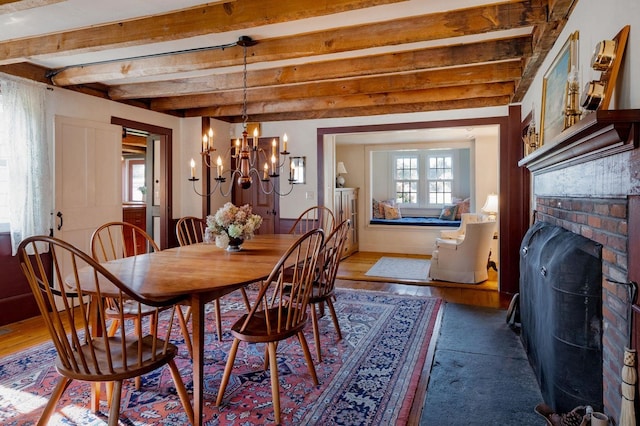 dining area with beam ceiling, a notable chandelier, a brick fireplace, and hardwood / wood-style flooring