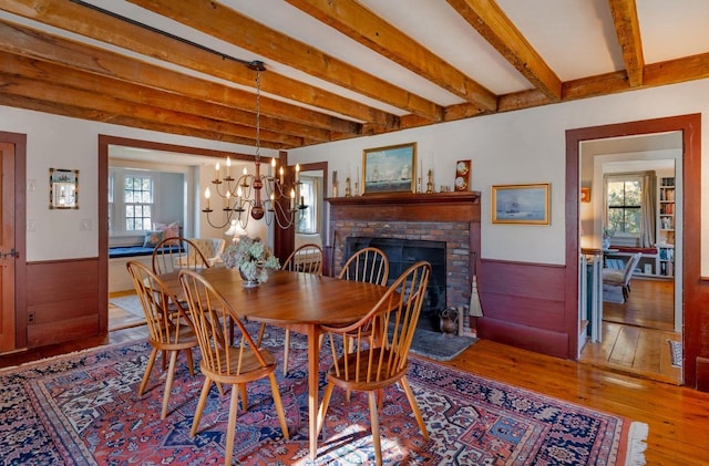 dining area with light hardwood / wood-style flooring, beamed ceiling, plenty of natural light, and a brick fireplace