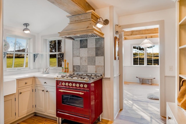 kitchen featuring lofted ceiling, backsplash, stainless steel stove, custom exhaust hood, and light hardwood / wood-style floors