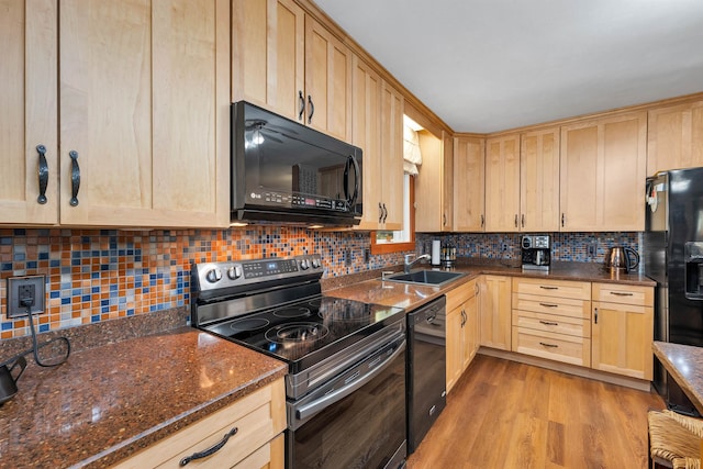 kitchen with sink, dark stone countertops, light hardwood / wood-style floors, decorative backsplash, and black appliances