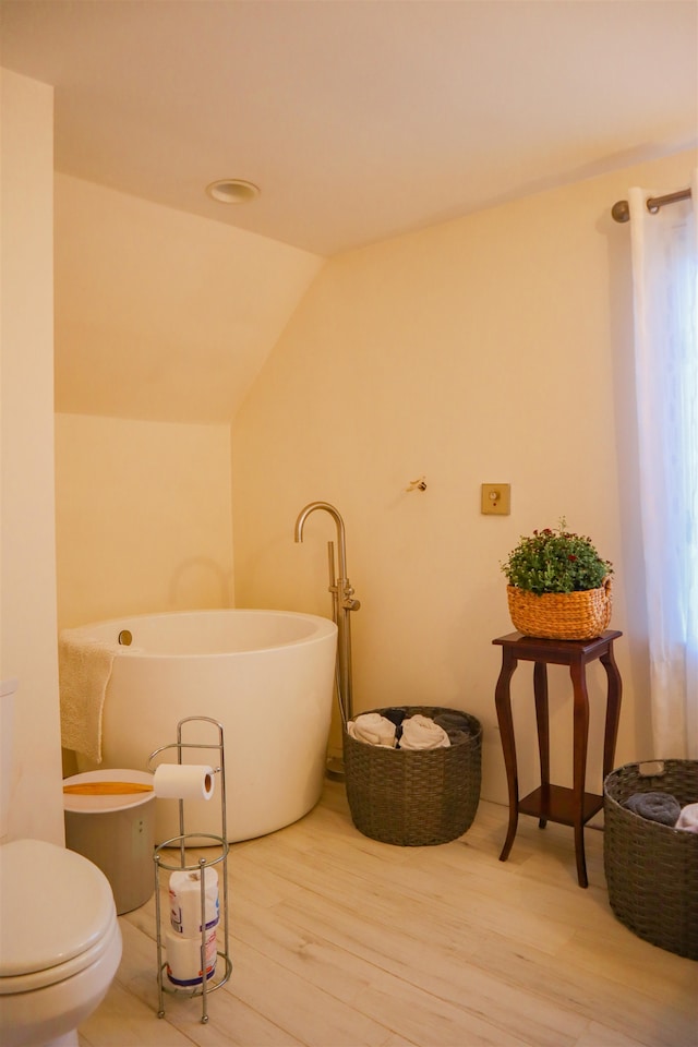 bathroom with lofted ceiling, wood-type flooring, toilet, and a washtub