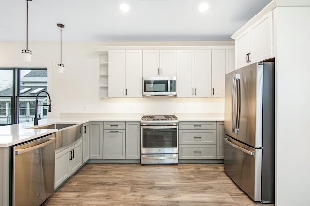 kitchen featuring appliances with stainless steel finishes, light hardwood / wood-style flooring, sink, gray cabinetry, and decorative light fixtures