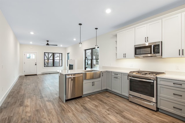 kitchen featuring kitchen peninsula, stainless steel appliances, sink, light hardwood / wood-style floors, and decorative light fixtures