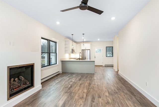 unfurnished living room featuring baseboard heating, dark wood-type flooring, and ceiling fan