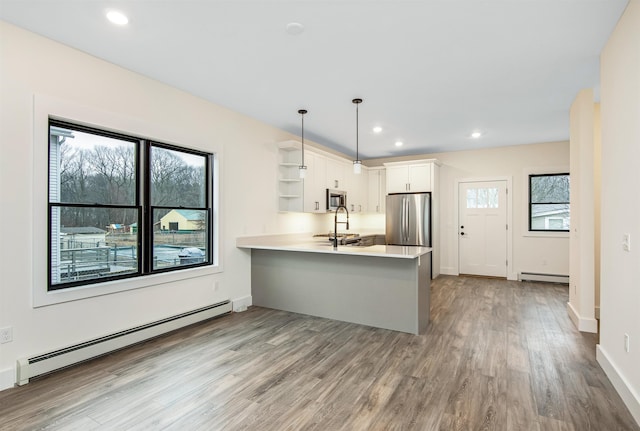 kitchen with baseboard heating, kitchen peninsula, a healthy amount of sunlight, decorative light fixtures, and appliances with stainless steel finishes