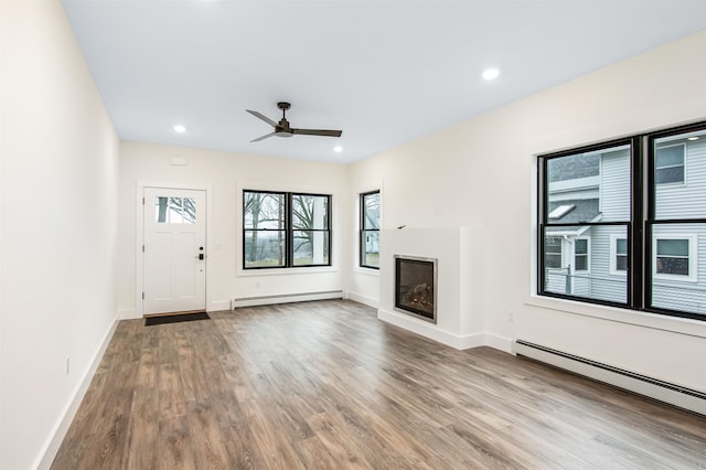 unfurnished living room featuring ceiling fan, baseboard heating, and hardwood / wood-style floors