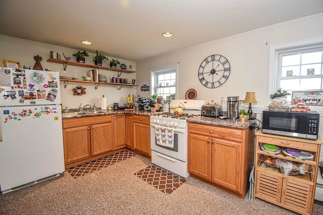 kitchen with a wealth of natural light, sink, white appliances, and dark stone countertops