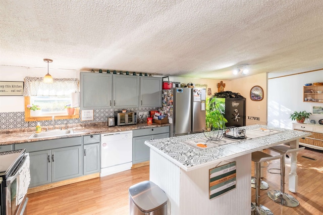 kitchen with backsplash, appliances with stainless steel finishes, hanging light fixtures, and light wood-type flooring