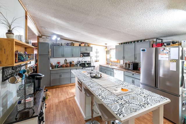 kitchen with appliances with stainless steel finishes, a textured ceiling, light wood-type flooring, vaulted ceiling, and sink