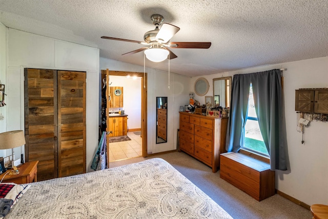 carpeted bedroom with a textured ceiling, ensuite bathroom, and ceiling fan