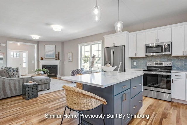 kitchen featuring stainless steel appliances, white cabinetry, pendant lighting, and light wood-type flooring