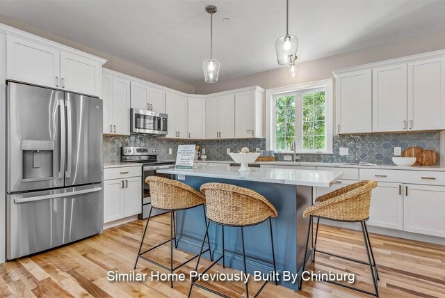 kitchen with decorative light fixtures, stainless steel appliances, a breakfast bar, and white cabinets