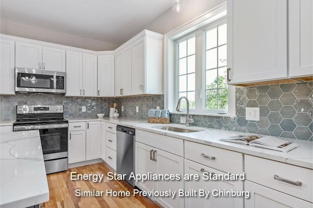 kitchen with appliances with stainless steel finishes, sink, white cabinets, and light stone counters