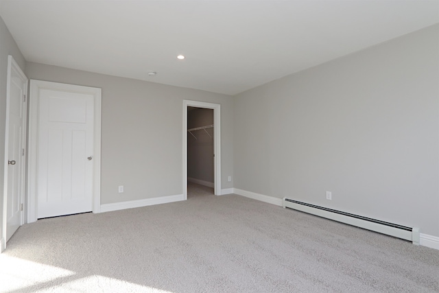 unfurnished bedroom with a baseboard radiator, a walk in closet, a closet, and light colored carpet