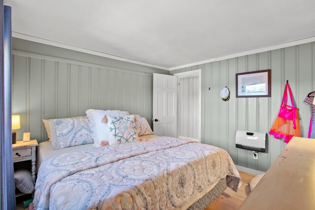 bedroom with crown molding, hardwood / wood-style floors, and wood walls