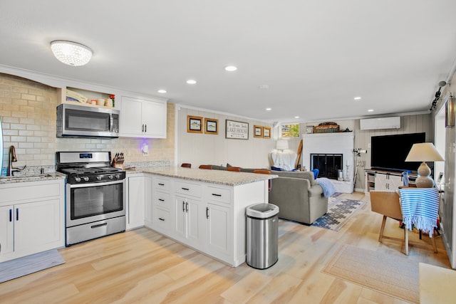 kitchen with appliances with stainless steel finishes, a wall mounted air conditioner, kitchen peninsula, white cabinetry, and light hardwood / wood-style floors