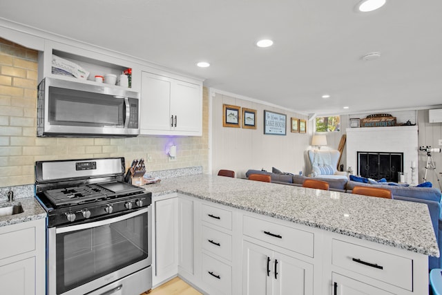 kitchen featuring kitchen peninsula, light stone counters, white cabinetry, light wood-type flooring, and stainless steel appliances