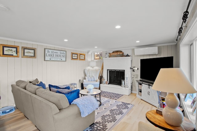 living room with a wall mounted AC, wooden walls, light hardwood / wood-style flooring, ornamental molding, and a brick fireplace