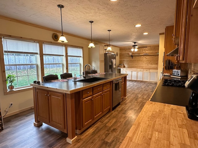 kitchen featuring a kitchen island with sink, wooden walls, sink, decorative light fixtures, and appliances with stainless steel finishes