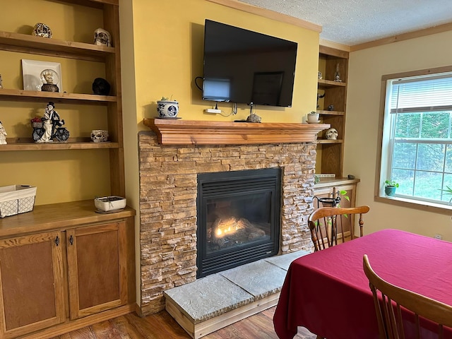 living room with hardwood / wood-style floors, a textured ceiling, ornamental molding, built in features, and a stone fireplace