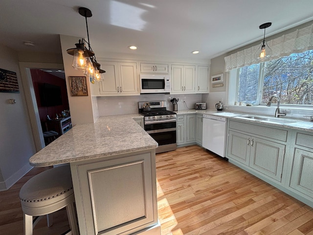 kitchen with hanging light fixtures, sink, kitchen peninsula, and white appliances