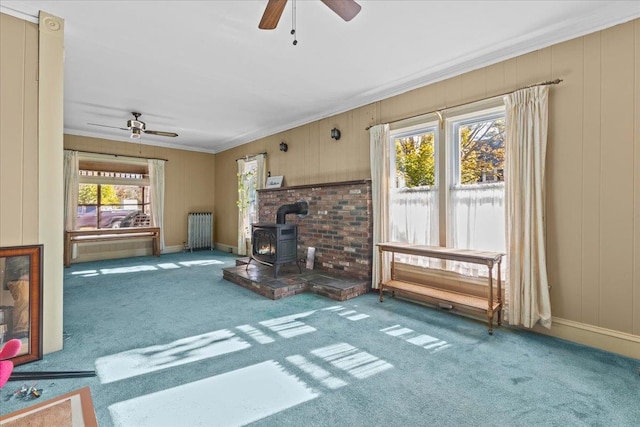 living room featuring a wood stove, radiator heating unit, carpet flooring, and a wealth of natural light