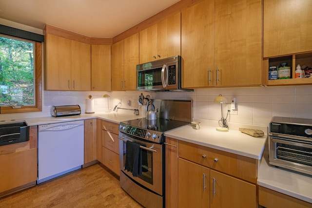 kitchen with backsplash, sink, stainless steel appliances, and light hardwood / wood-style flooring