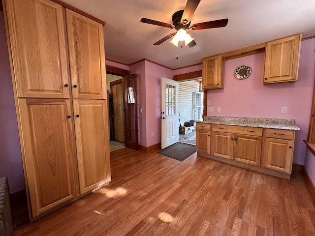 kitchen with crown molding, light stone counters, light wood-type flooring, and ceiling fan