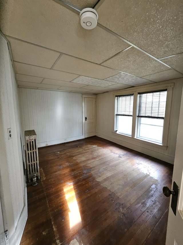 unfurnished room featuring a drop ceiling, dark hardwood / wood-style floors, and wooden walls