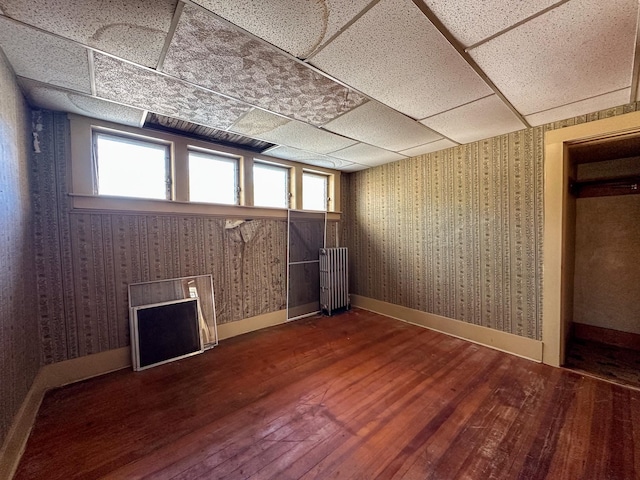 basement featuring radiator heating unit, a paneled ceiling, hardwood / wood-style floors, and plenty of natural light