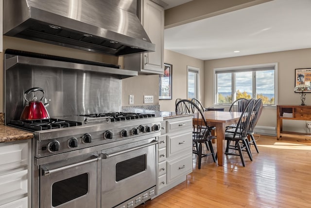 kitchen with white cabinetry, wall chimney range hood, light hardwood / wood-style flooring, and double oven range