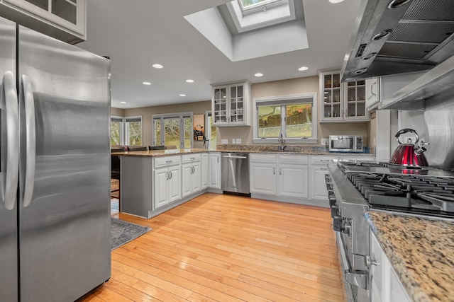 kitchen featuring white cabinets, appliances with stainless steel finishes, light hardwood / wood-style flooring, a skylight, and ventilation hood